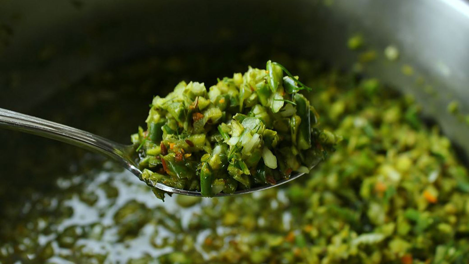 Dilly garlic scape relish on a spoon over a bowl of relish.