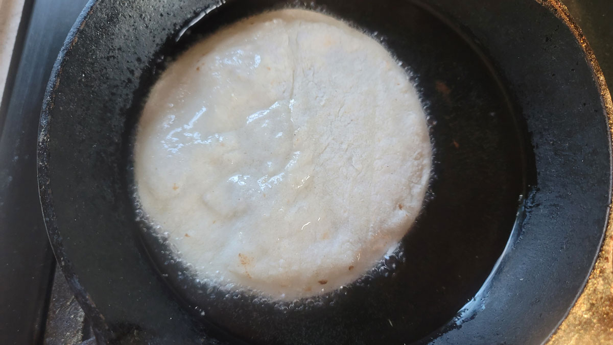 Tortilla in a small cast iron pan with bubbling oil.