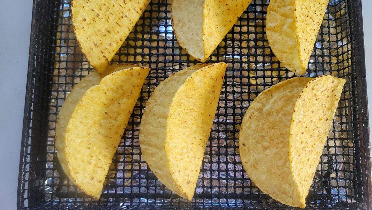 Hard taco shells arranged in an air fryer basket.