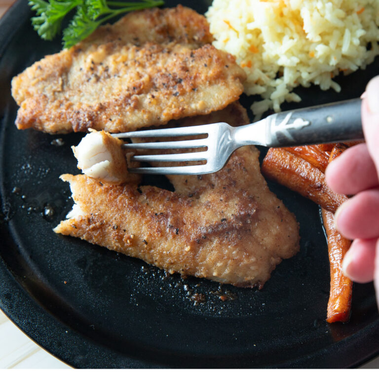 Fork flaking off a piece of fish.