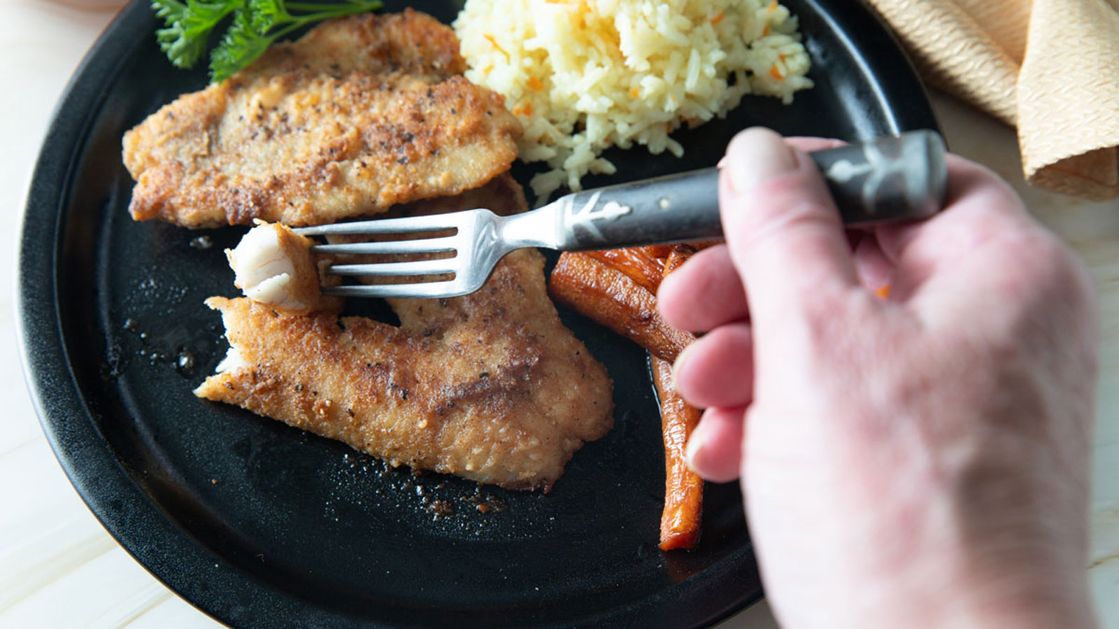 Woman's hand breaking off a piece of flaky largemouth bass.