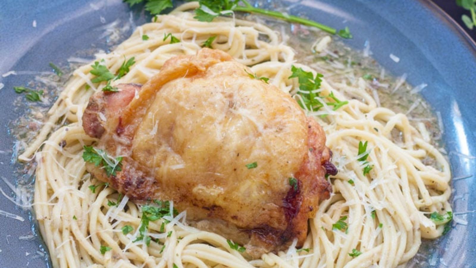 lemon chicken atop pasta on blue plate