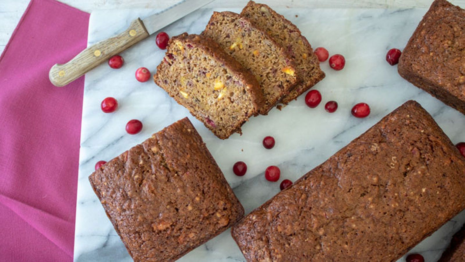 Slices of Orange Cranberry Pumpkin Quick Bread next to whole loaves