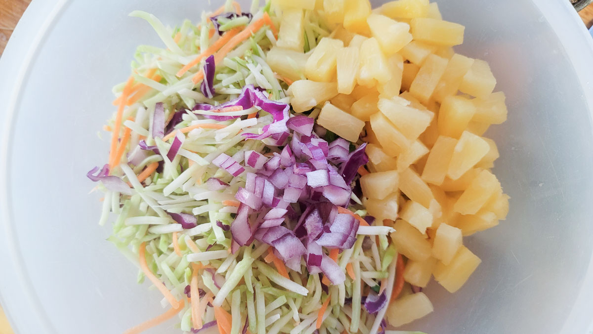 Cabbage, onion and pineapple added to a large bowl.