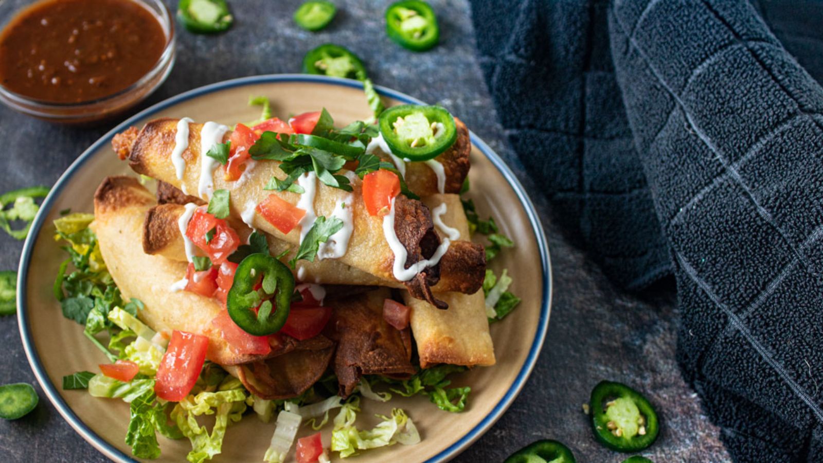 Pile of taquitos garnished with creme and vegetable.