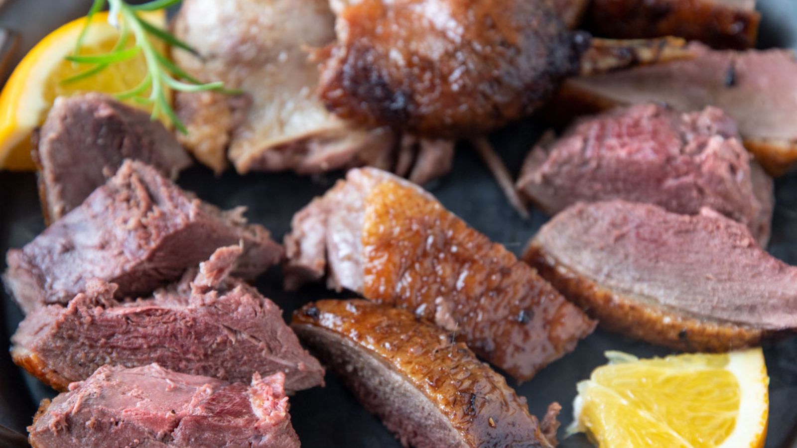 Sliced roast duck on pewter plate with orange slices.