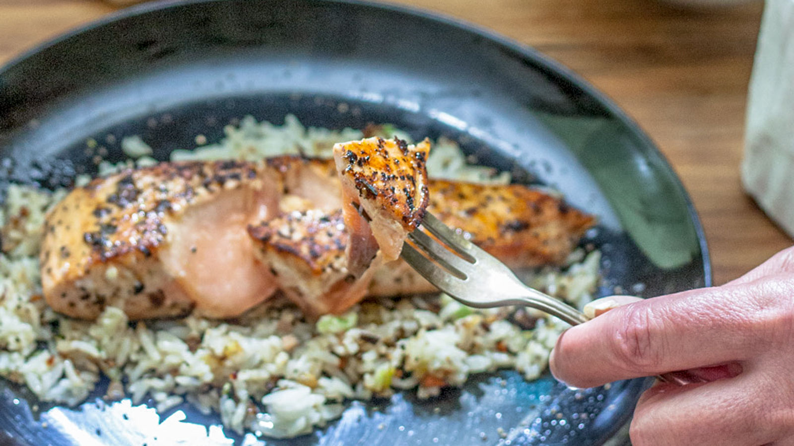 Seared salmon held on fork by woman's hand.