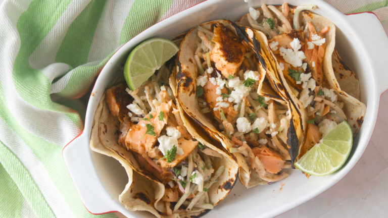 Three salmon tacos served in a white bowl with a lime wedge.