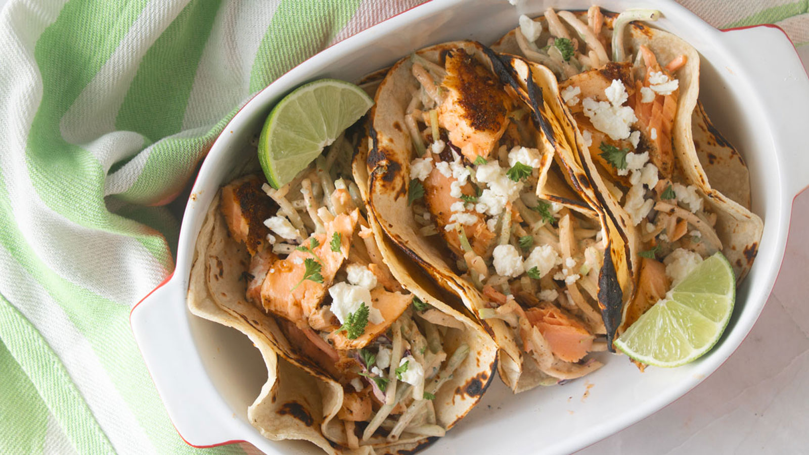 Three salmon tacos served in a white bowl with a lime wedge.