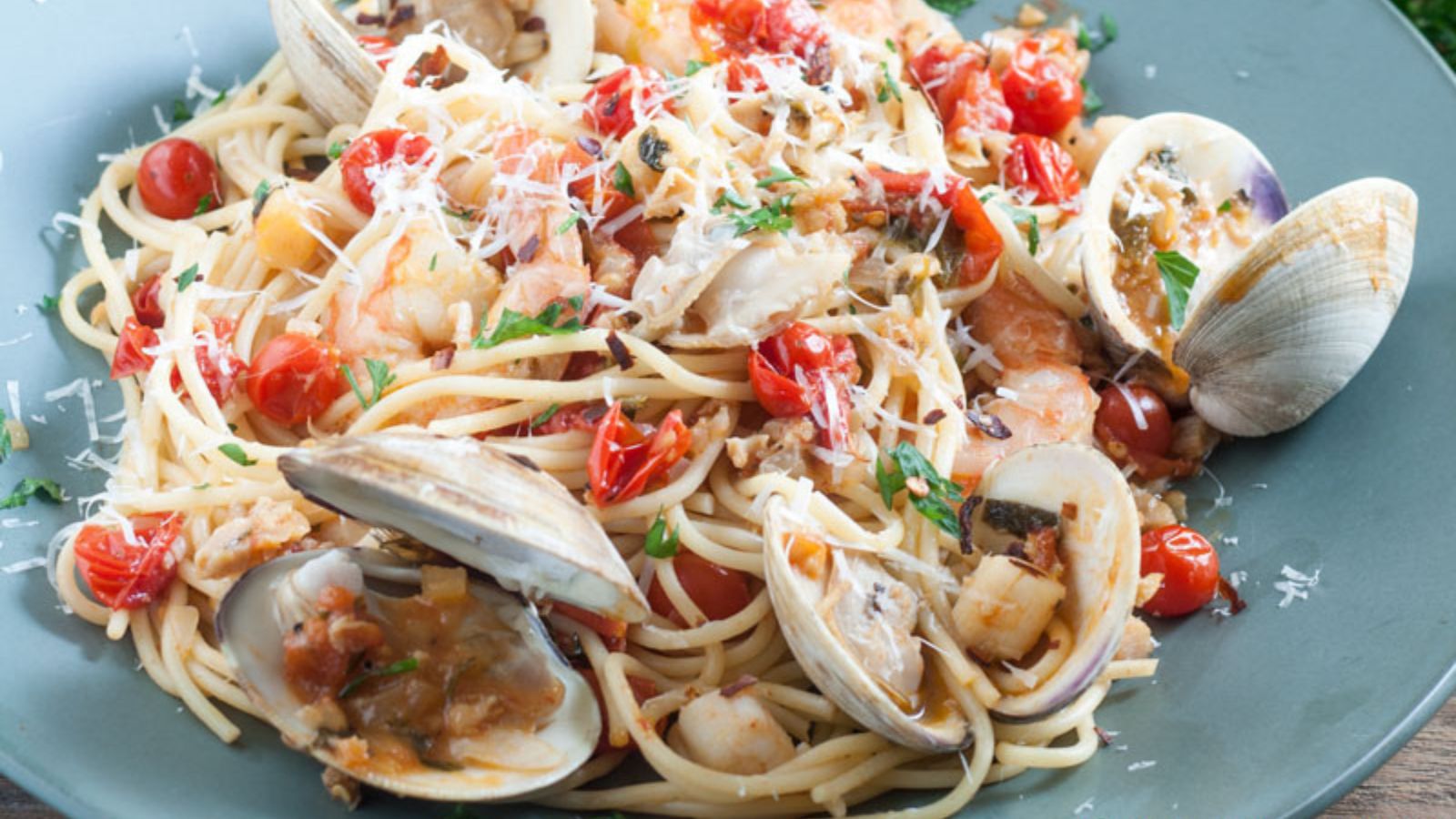 clams, shrimp, scallops in a fresh cherry tomato sauce on blue plate