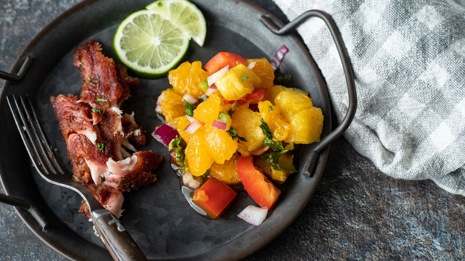 Individual portion of smoked catfish with citrus salsa and lime slices.