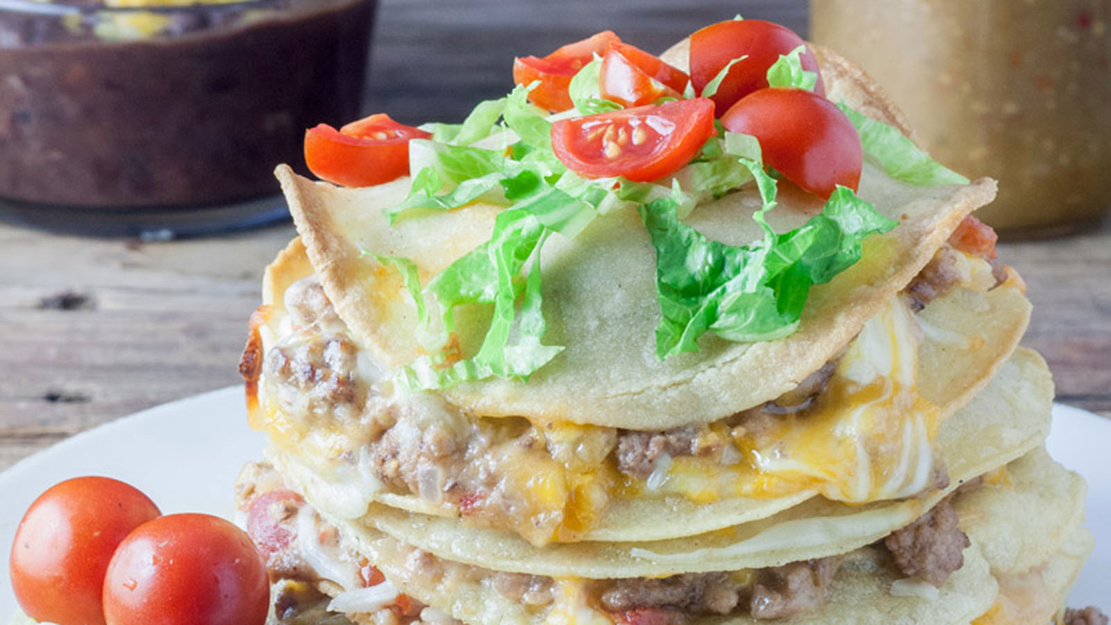 Stacked enchiladas topped with shredded lettuce and chopped tomatoes.