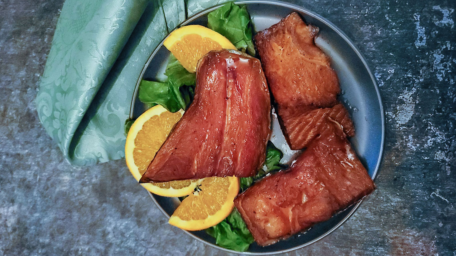 Glistening pieces of trout on gray plate with orange garnish.