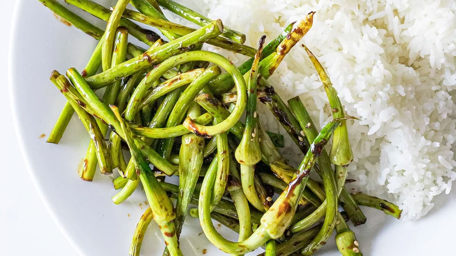 Stir fried garlic scapes on a white plate with rice.