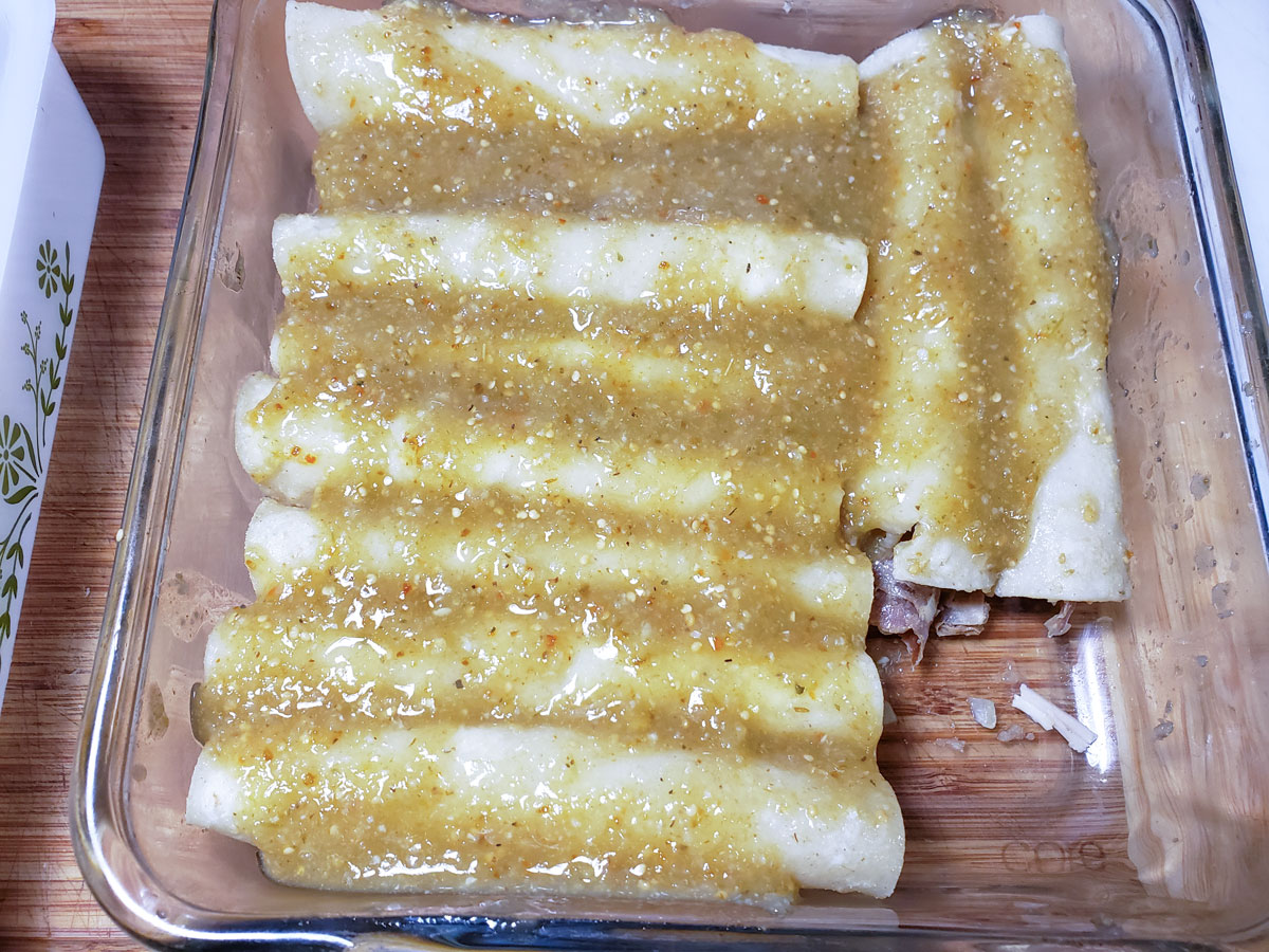 All of the enchiladas in a casserole dish covered with sauce.