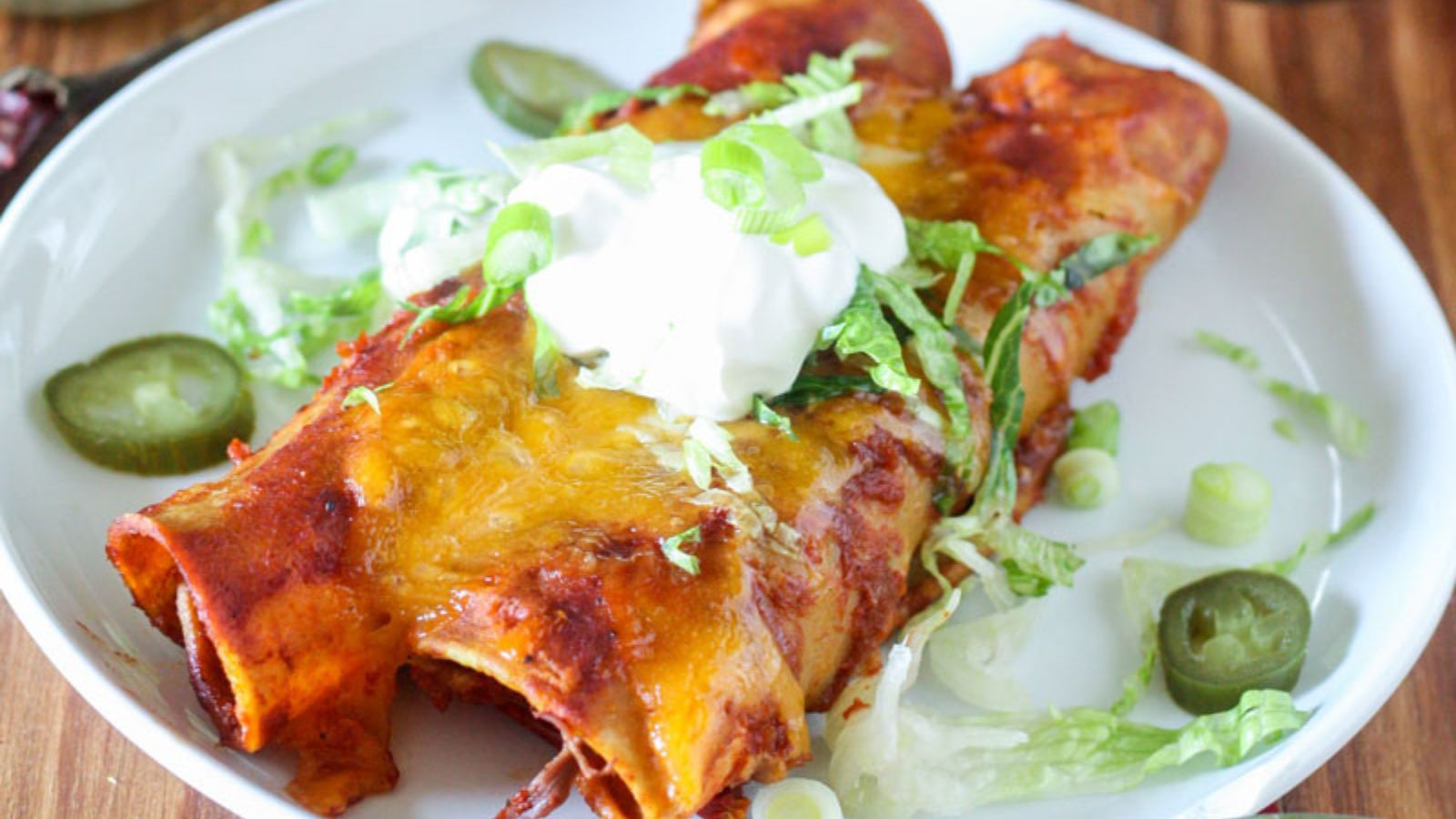 Two enchiladas on white plate with sour cream and lettuce on top