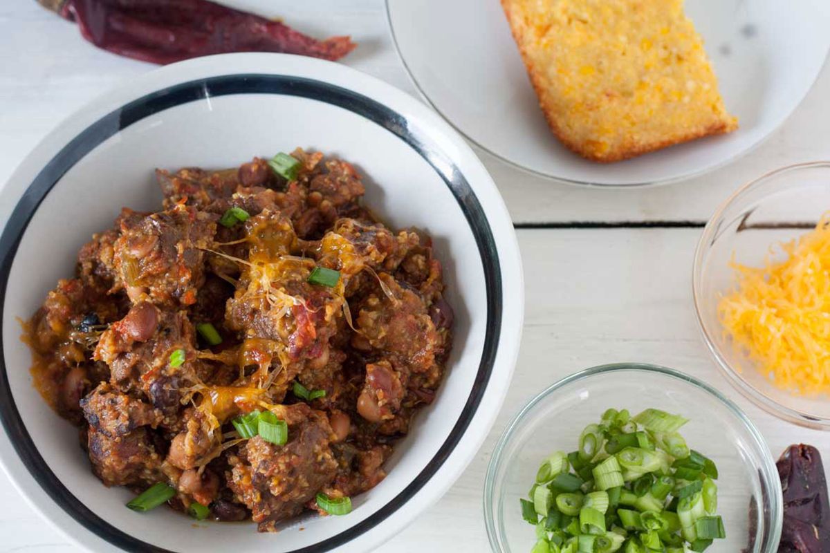 Bowl of venison chili topped with cheddar cheese and served with corn bread.