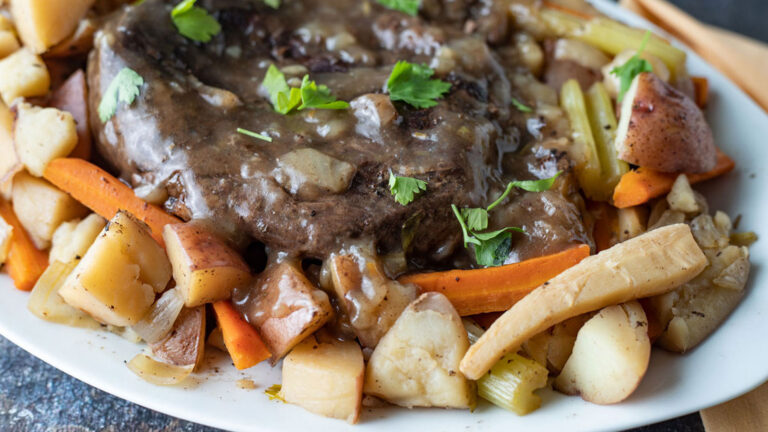 Venison roast smothered in gravy on a platter with roasted root vegetables.