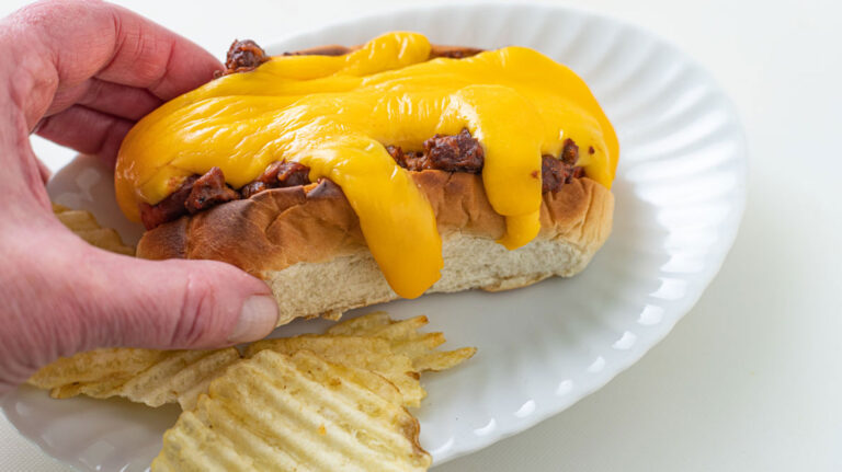 Woman's hand grabbing a hot dog on a bun with melted cheese.