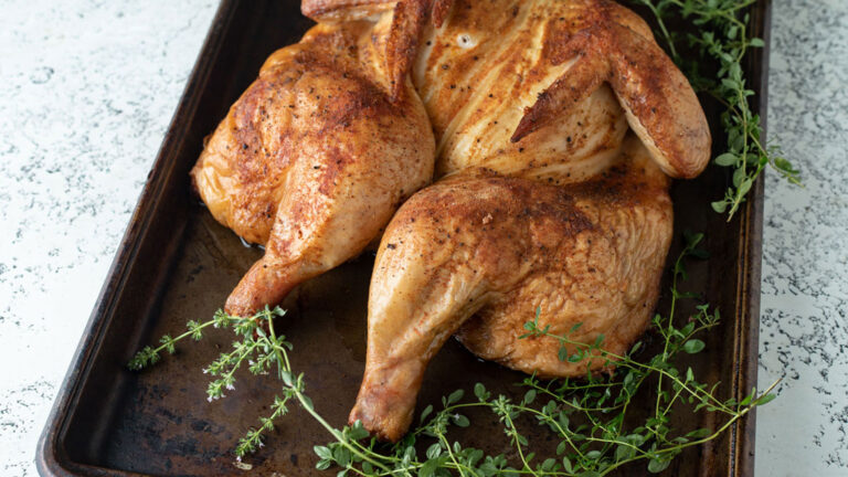 Golden spatchcocked chicken on a rimmed baking sheet.