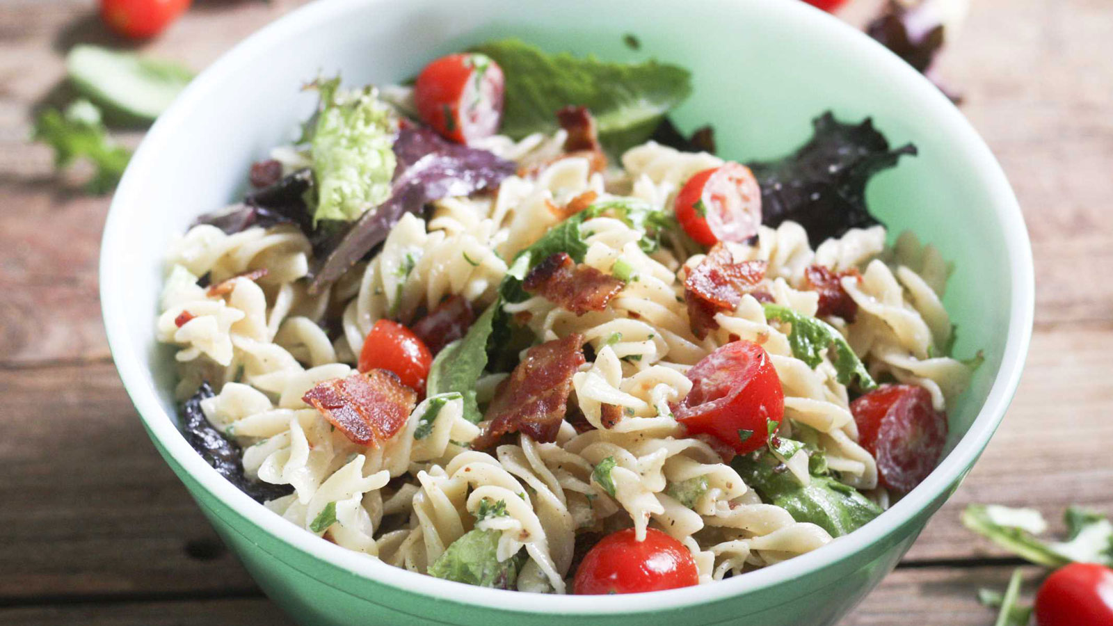 BLT pasta salad in green bowl with colorful tomatoes.