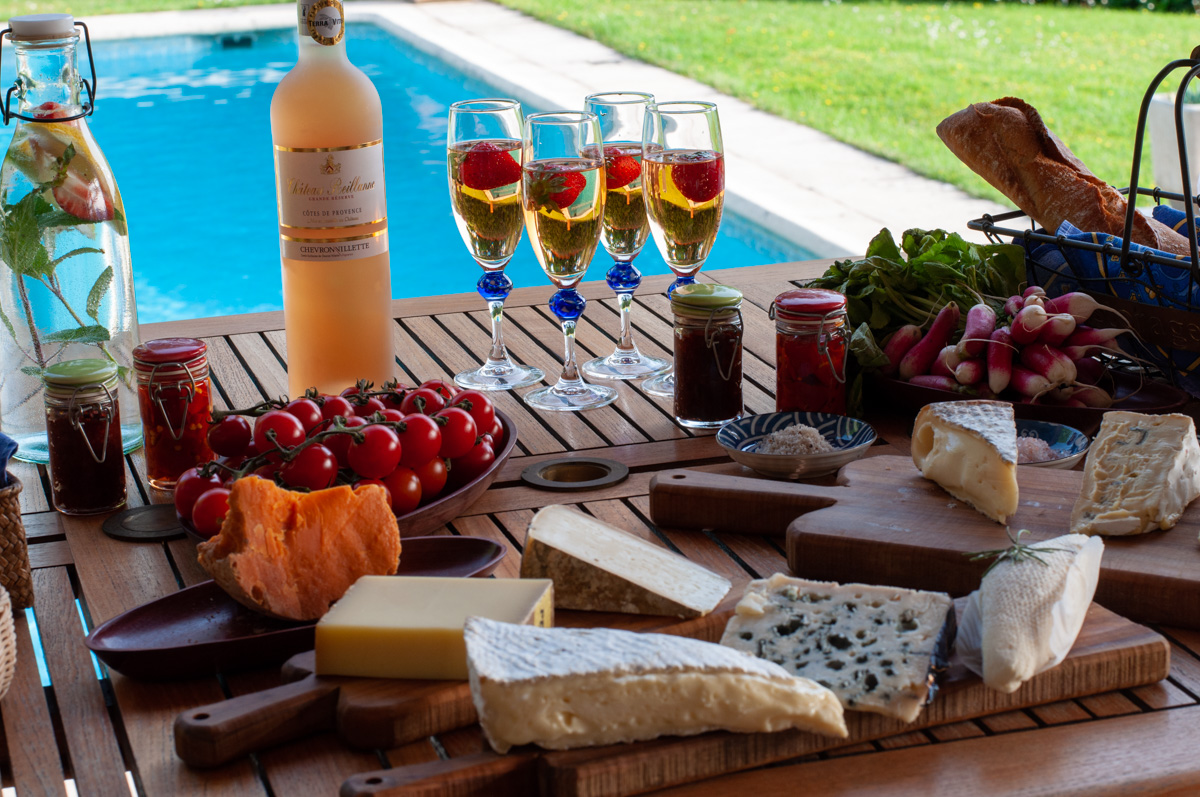 French cheeses and wine on table by a pool.