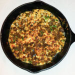 Browned chorizo with melted cheese and peppers in a cast iron skillet.