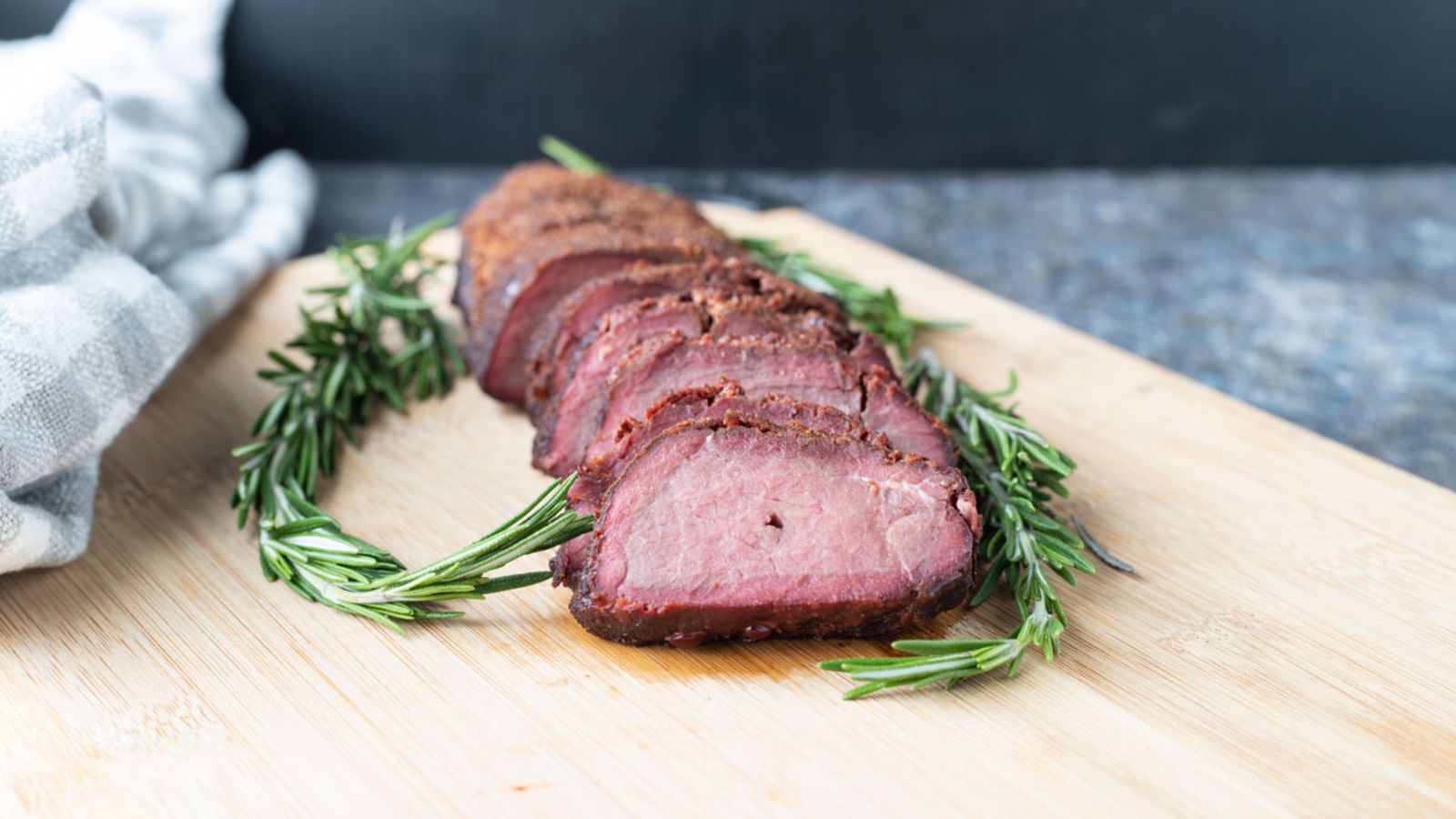 Sliced backstrap on board with fresh rosemary garnish.