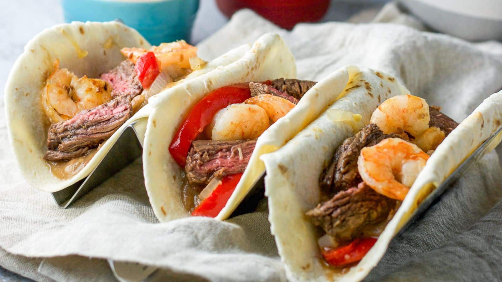 Three pieces of tacos with shrimp and steak on a plate.