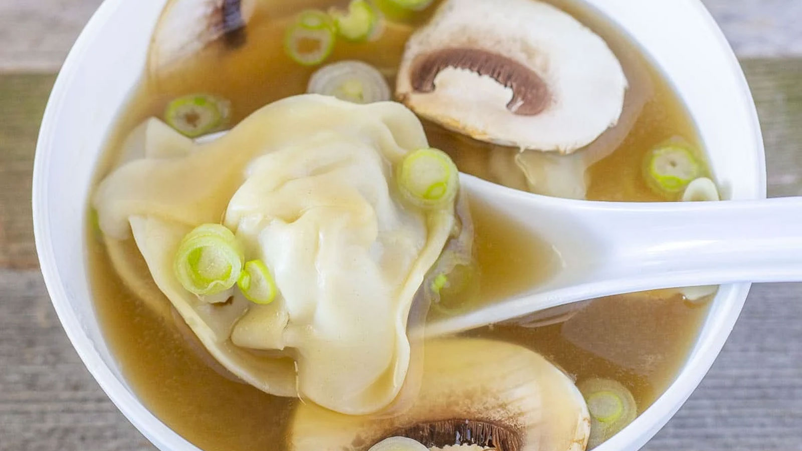 Spoon grabbibg a wonton from the broth.