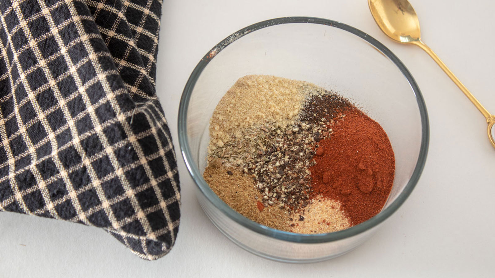 Spices in a glass bowl with a gold spoon.