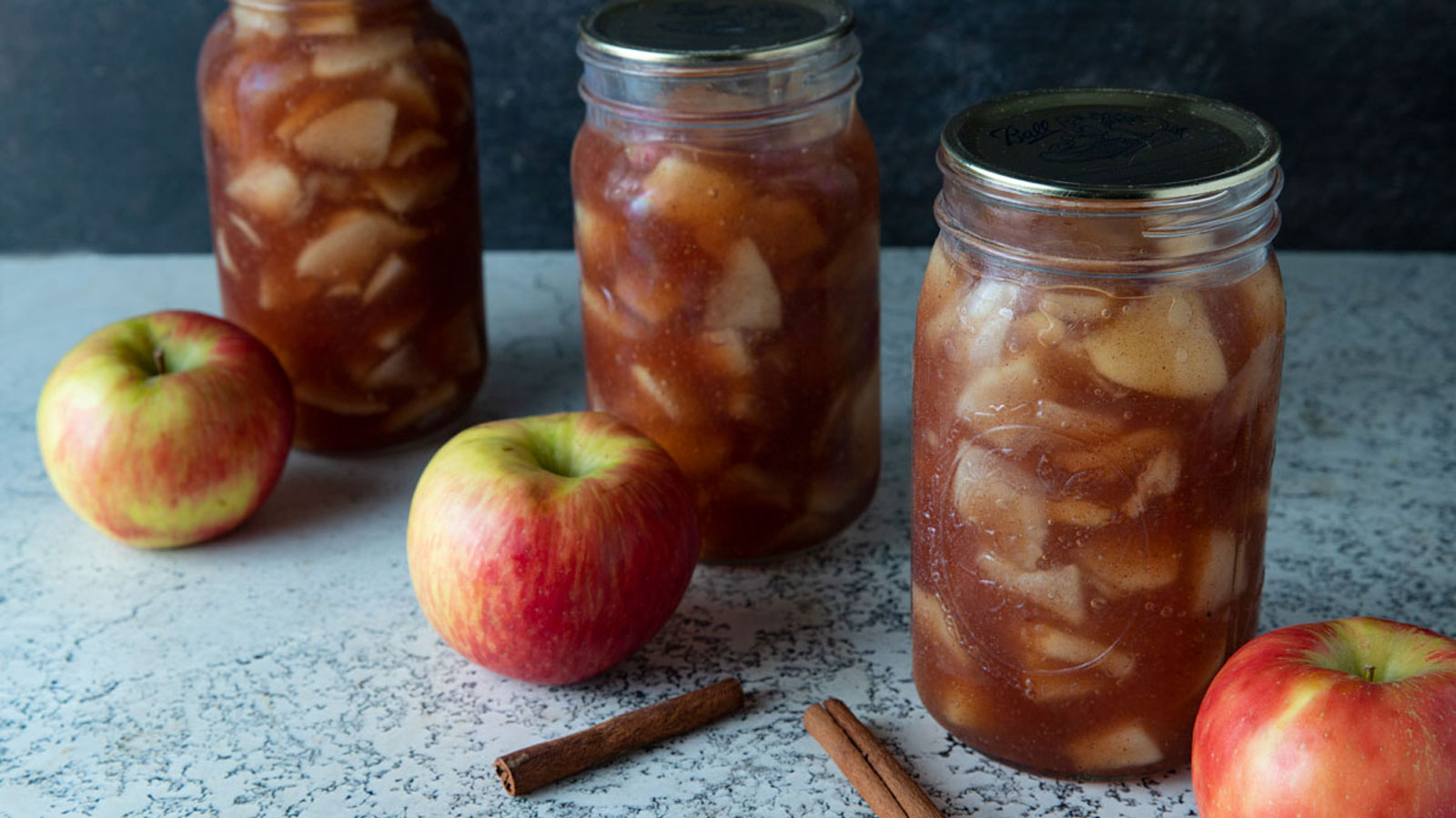 Apple pie filling in jars with fresh apples next to the jar.