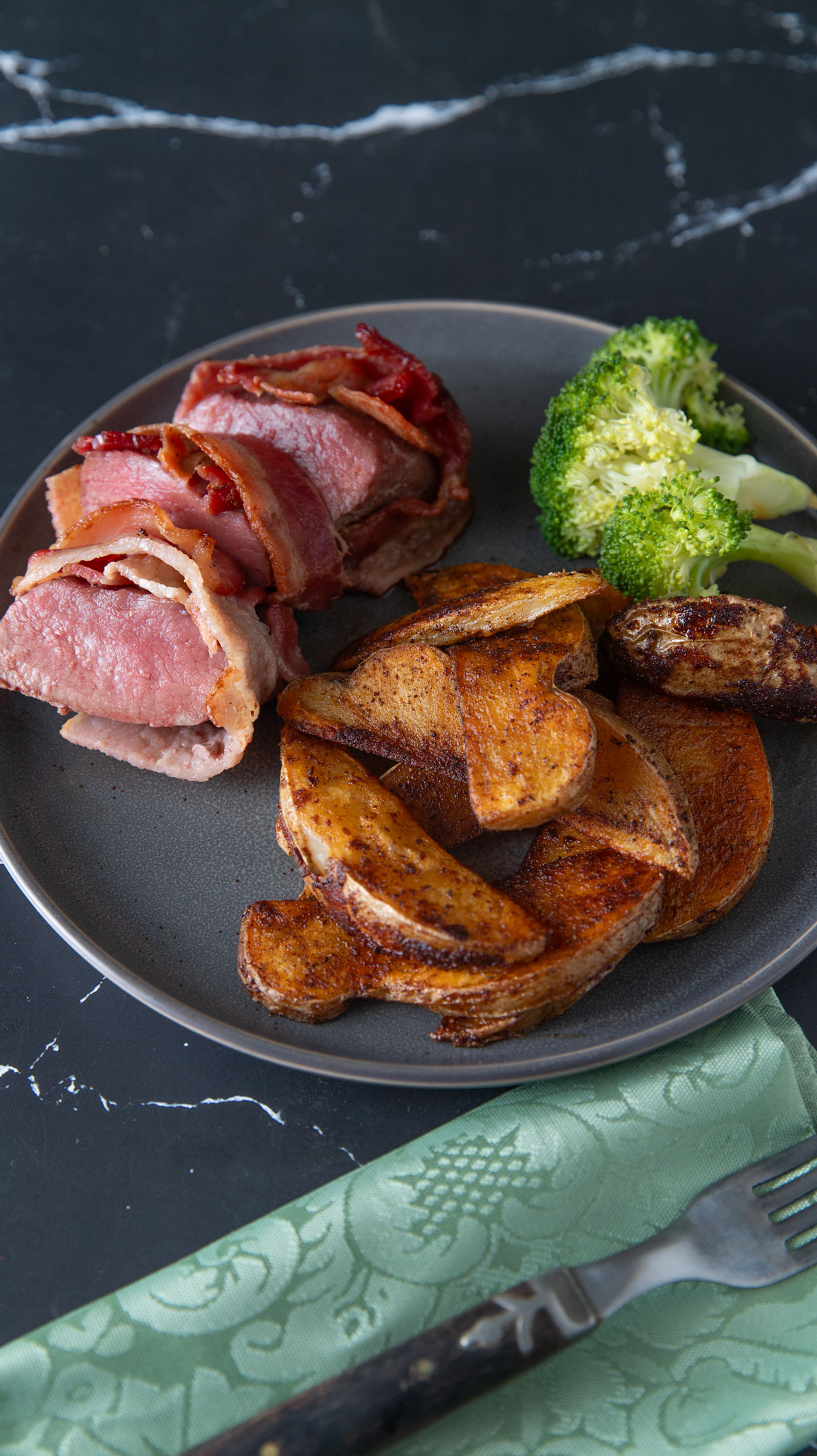 Slices of Venison loin wrapped in bacon served with sides.
