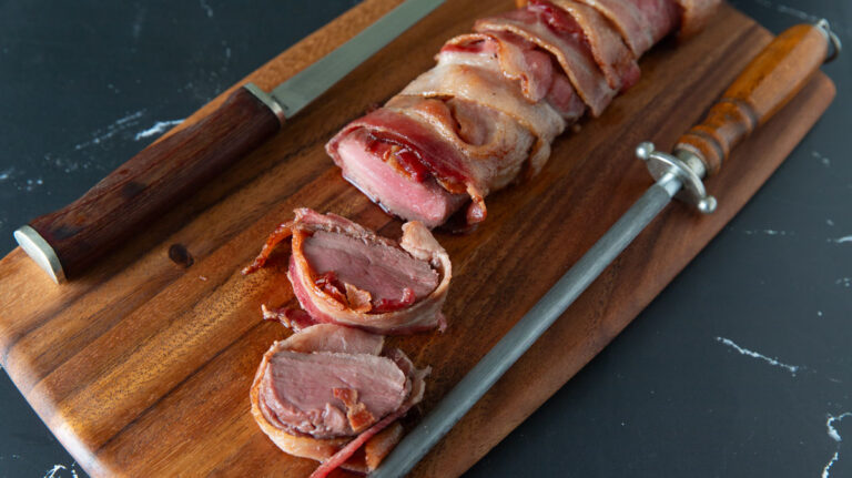 sliced bacon wrapped venison on a wooden board.