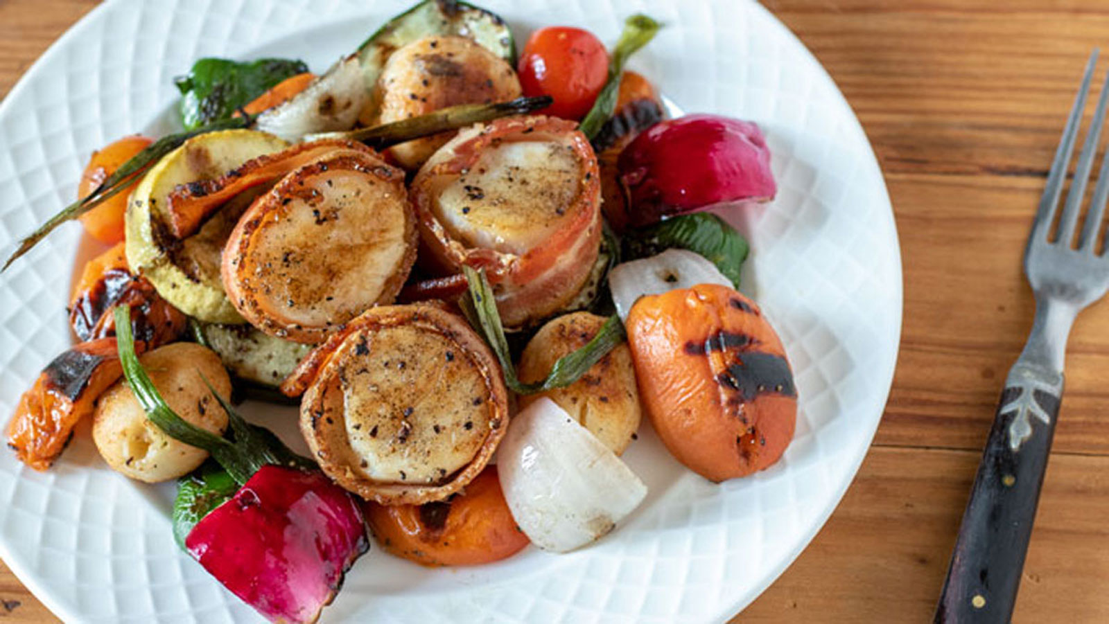 Vegetables and bacon wrapped scallops on white plate