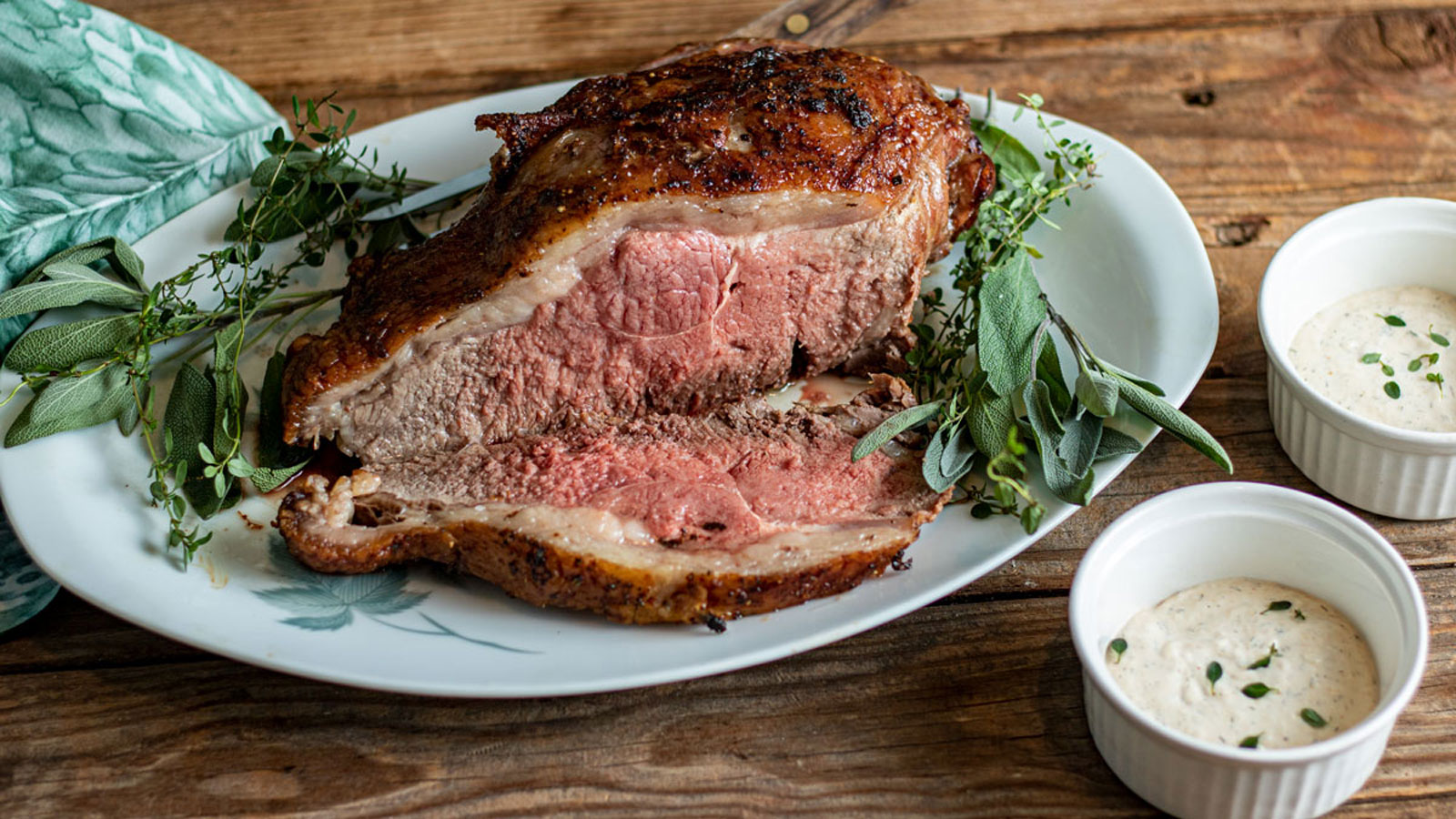 Sliced beef strip loin on a plate with veggies and dip on the side.