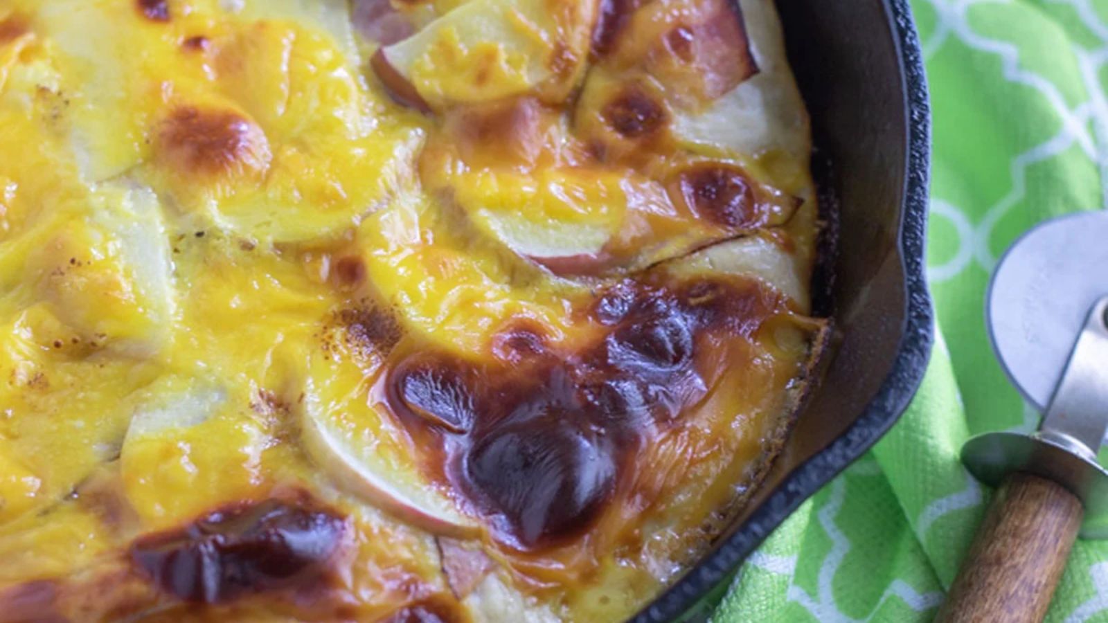 Breakfast pizza in a cast iron pan with a pizza cutter.