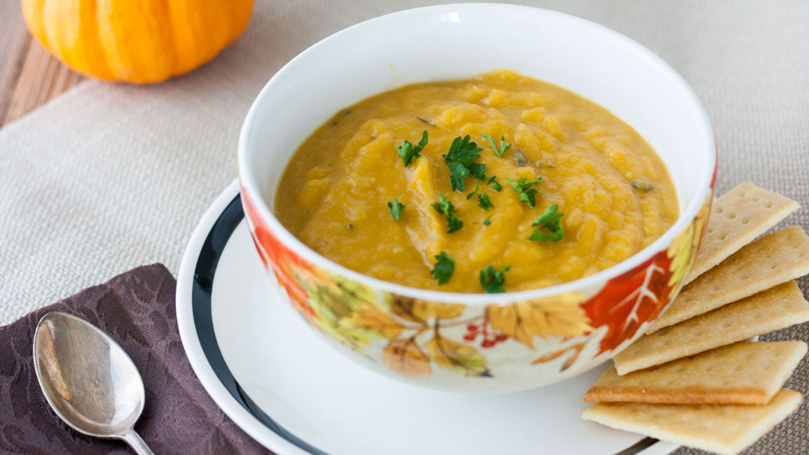 Butternut soup in a fall themed bowl garnished with chopped parsley.