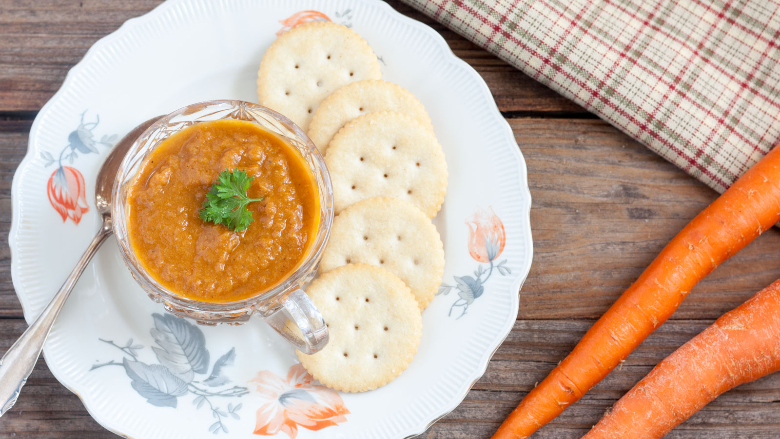 Carrot soup in a cup with crackers on a plate.