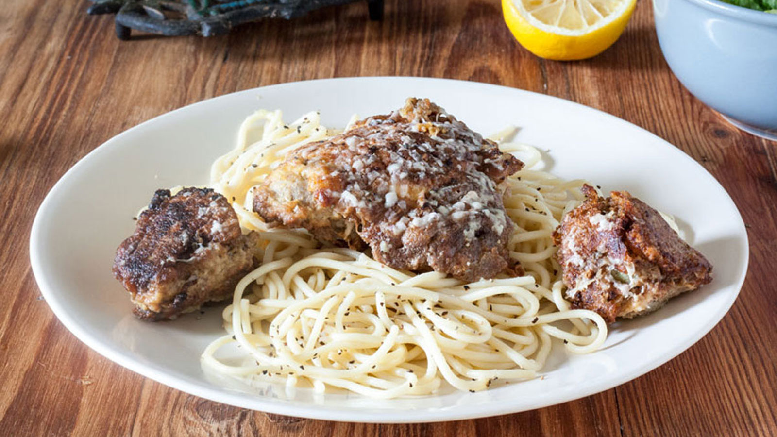 Chicken French topped spaghetti on a white bowl.