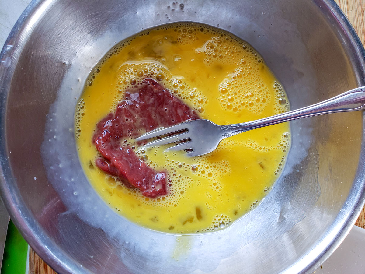 Dipping a steak into egg wash.