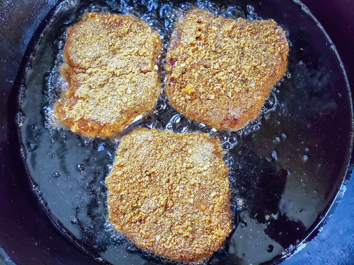 Breaded steaks in a cast iron skillet.