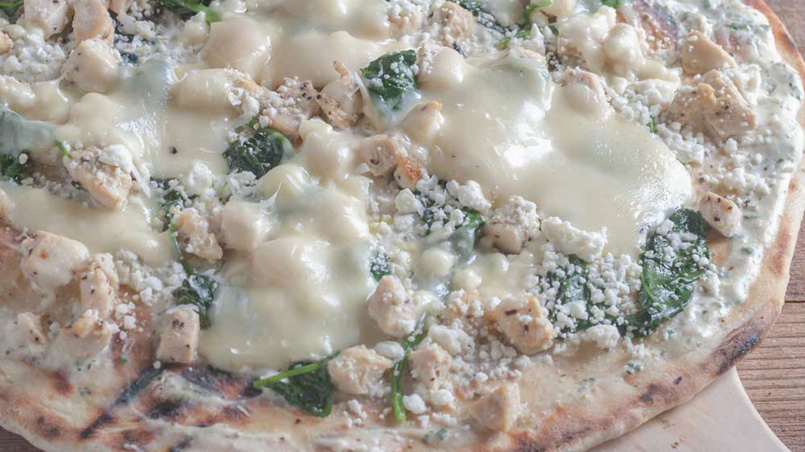 Close up of chicken pizza with spinach and cheeses.