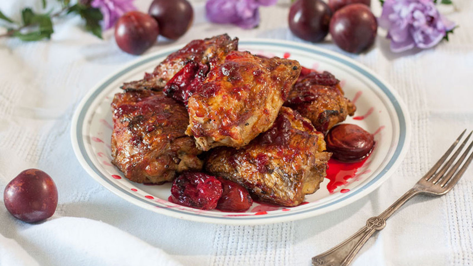 Pile of chicken and plums on a white plate.