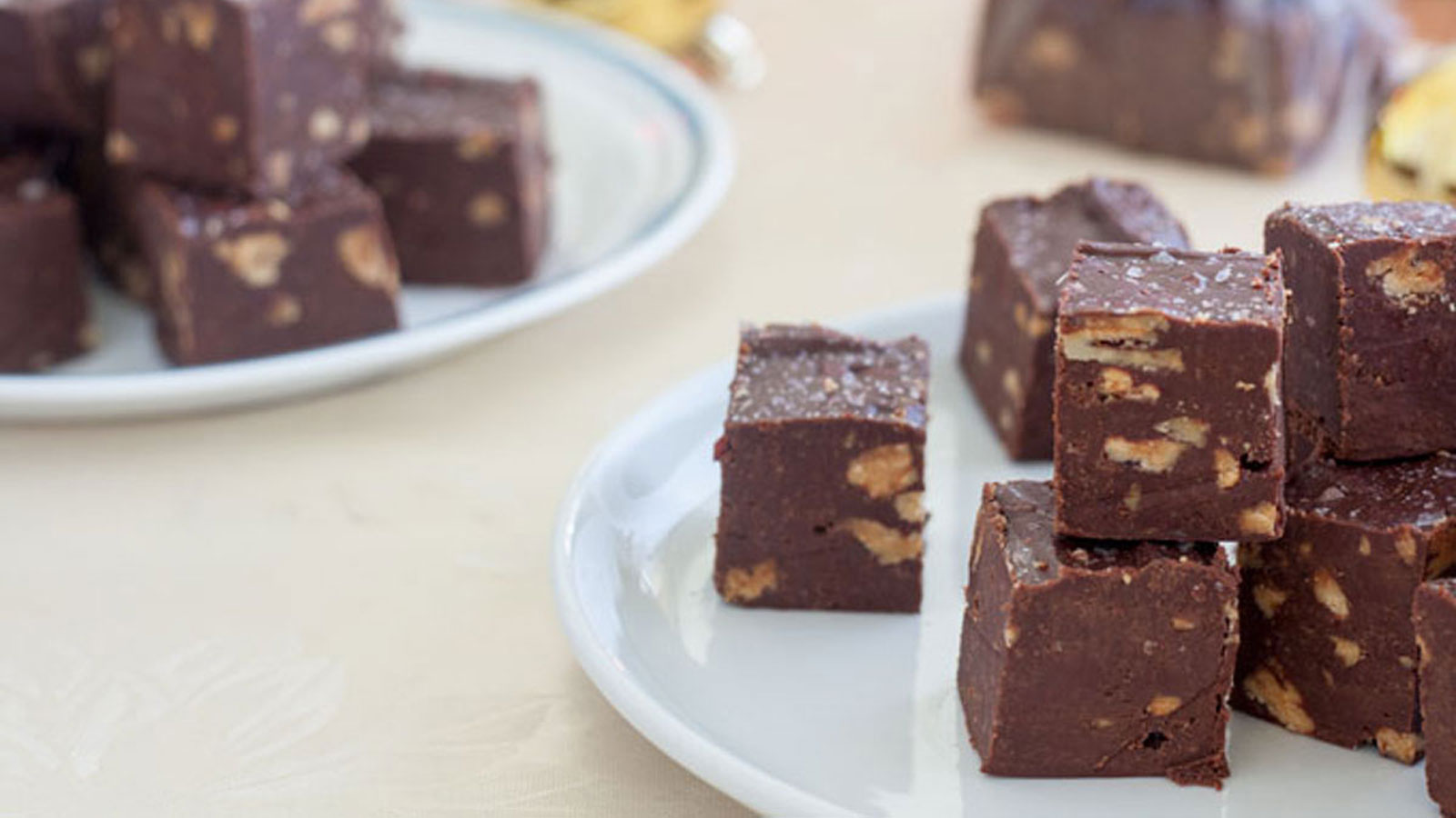 Chocolate fudge on white plates with Christmas decorations in photo.