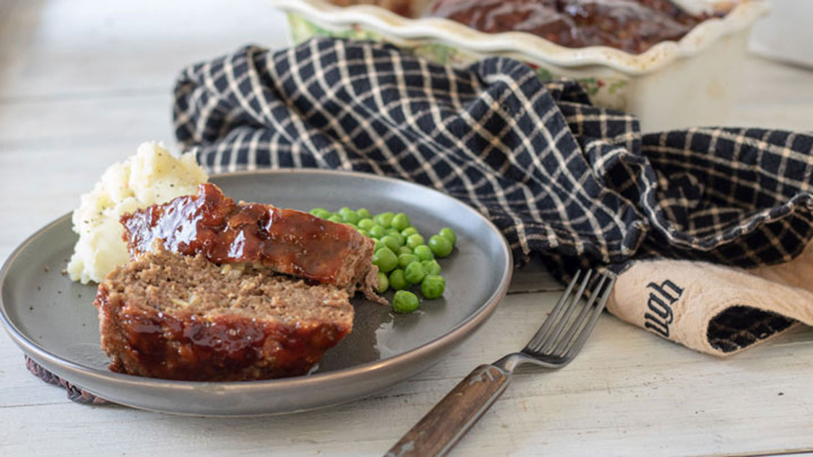 Two slices of meatloaf on grey plate with mashed potatoes and peas.