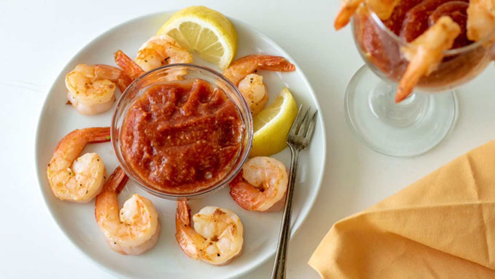 bowl of cocktail sauce on a white plate surrounded by shrimp.