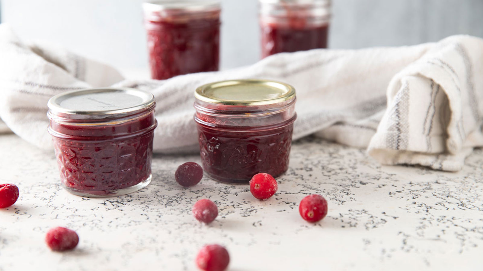 Jars of cranberry butter with fresh cranberries on white board.