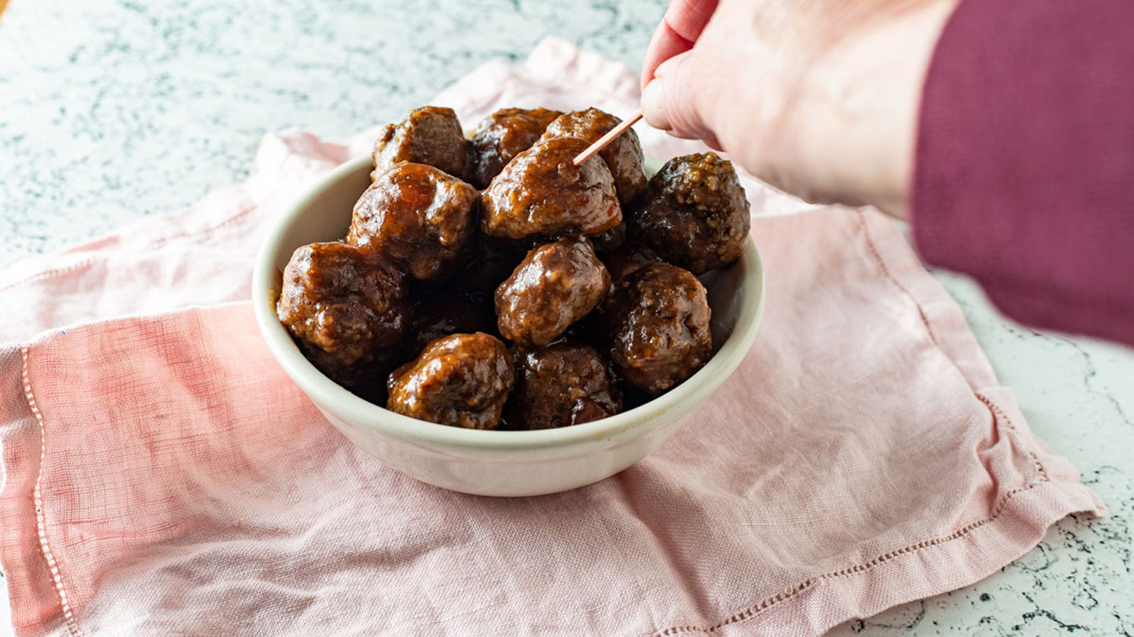 Woman's hand stabbing meatball with toothpick from bowl.