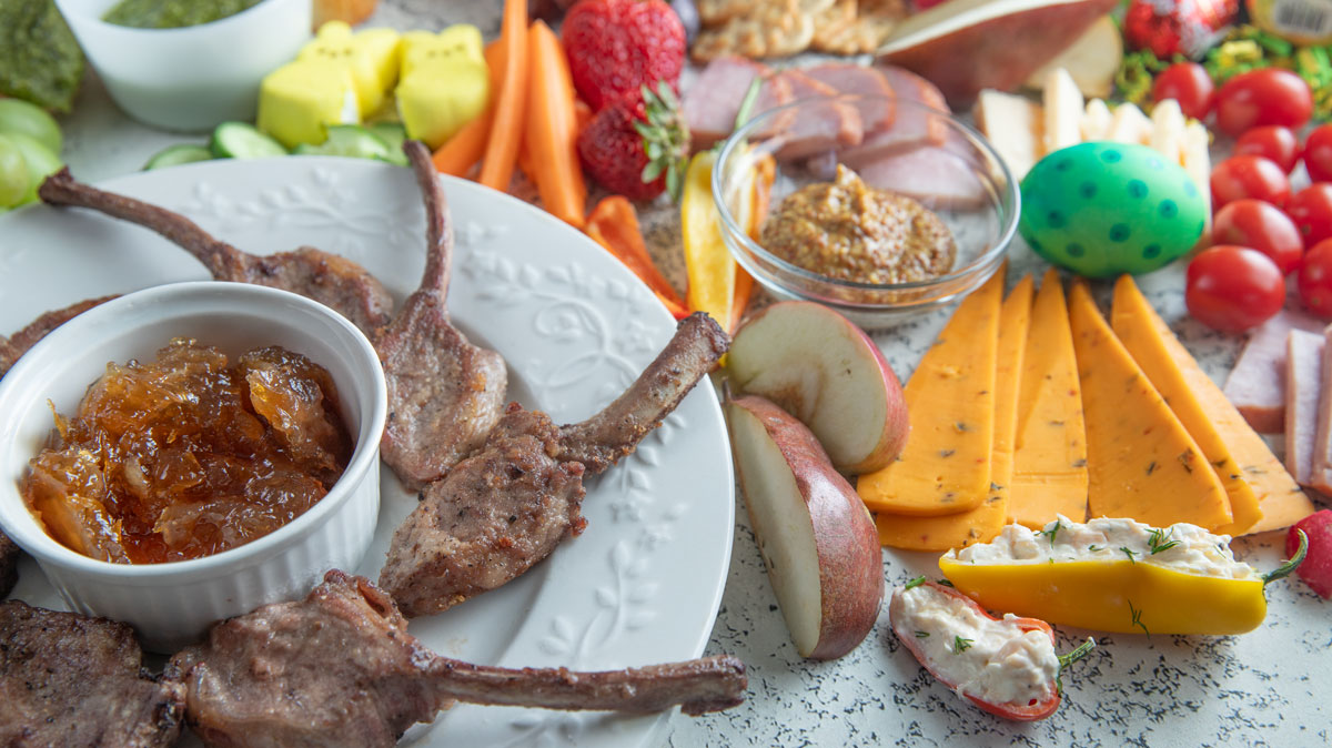 Plate with French cut lamb chops and cut cheeses and fruit.